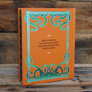 Puede incluir: La cubierta trasera de un libro con un fondo naranja y un dise&ntilde;o de serpiente verde. El texto en la cubierta dice "THAT IS MEDUSA. DO NOT LOOK AT HER! THE SIGHT WOULD TURN YOU TO STONE!"