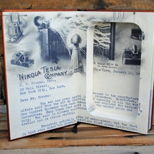 May include: A vintage letter from Nikola Tesla Company to J.P. Morgan, dated January 10, 1919, discussing the importance of nitric acid production during wartime. The letter is displayed in a book with a cut-out window revealing a vintage photograph of Tesla's inventions.