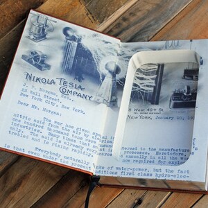 May include: A vintage book with a hidden compartment that reveals a photograph of Nikola Tesla's laboratory. The book's cover features the text "Nikola Tesla Company" and a letter addressed to J.P. Morgan. The letter discusses the importance of nitric acid in wartime industries.