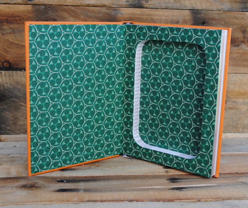 Puede incluir: Un libro naranja con una cubierta de patr&oacute;n verde est&aacute; abierto para revelar un compartimento oculto. El compartimento est&aacute; forrado con papel blanco y tiene un fondo de patr&oacute;n verde.