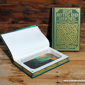 Puede incluir: Un libro verde con un diseño de nudo celta dorado en la portada. El libro está abierto para revelar un compartimento oculto en el interior. El título del libro es "Irish Myths and Legends: Ancient Tales of Gods, Goddesses and Otherworldly Folk".