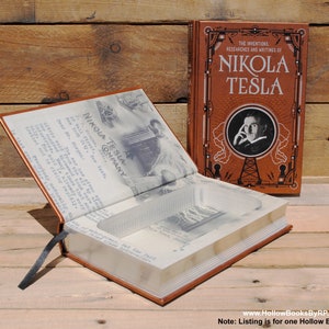 May include: An open book titled "The Inventions, Researches and Writings of Nikola Tesla" with a hidden compartment inside. The book is brown with gold lettering and a picture of Nikola Tesla on the front cover. The book is open to reveal a hollow space inside.
