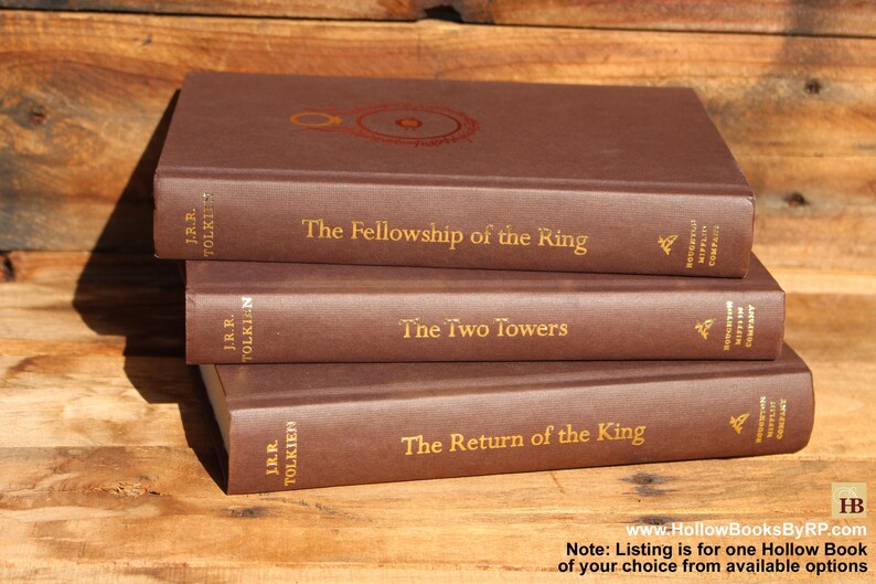 May include: Three brown hardback books stacked on a wooden surface. The titles are "The Fellowship of the Ring", "The Two Towers", and "The Return of the King" in gold lettering. The author's name, J.R.R. Tolkien, is also visible.