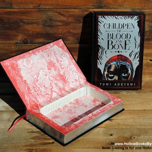 May include: A black book with a red and white map inside. The book cover features the title "Children of Blood and Bone" by Tomi Adeyemi.