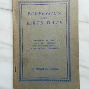 May include: A tan softcover booklet titled Profession and Birth Date by Donald A. Bradley. The cover features blue text and a decorative border, with the subtitle A Statistical Analysis of Planetary Positions at the Birthdates of 2492 Eminent Clergymen.