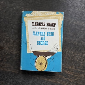 May include: A vintage paperback book titled "Martha, Eric and George" by Margery Sharp. The cover is light blue with a gold border and features an illustration of a baby carriage. The book's title and author's name are in bold, dark blue text.