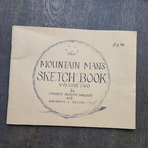 May include: A tan-colored sketchbook titled "The Mountain Man's Sketch Book, Volume Two." The cover features a circular design with the title in a decorative font. The authors' names are also listed. The price is $4.00.