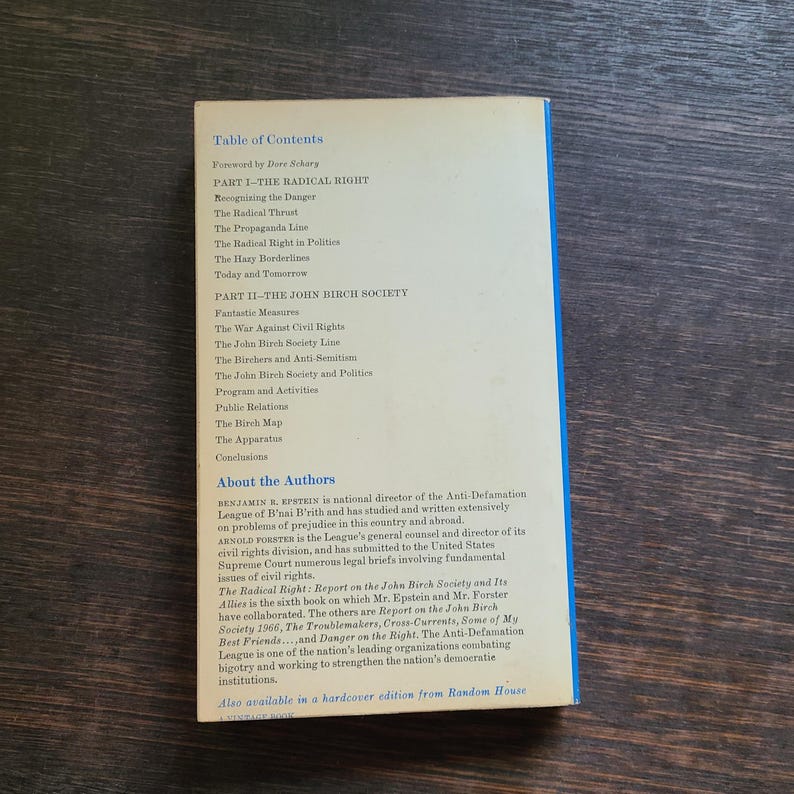 K&ouml;nnte beinhalten: Buchr&uuml;cken mit blauem Buchr&uuml;cken und wei&szlig;em Text auf cremefarbenem Hintergrund. Der Text enth&auml;lt ein Inhaltsverzeichnis, Autoreninformationen und den Titel "The Radical Right". Das Buch liegt auf einer Holzoberfl&auml;che.
