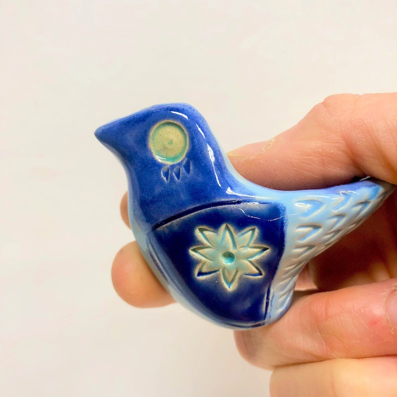 May include: A small blue and white ceramic bird with a flower design on its chest. The bird has a green eye and a white beak.