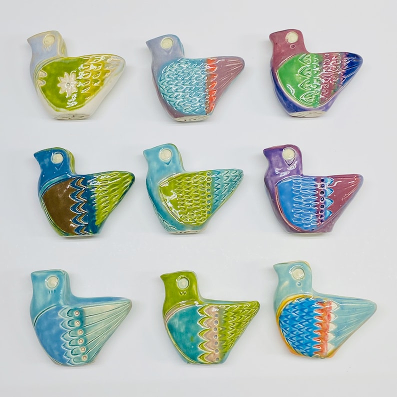 May include: Nine ceramic bird figurines with different coloured glazes and patterns. The birds are all facing the right side of the image. The birds are all in a row, with three birds in each row.