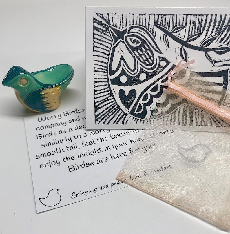 May include: A small ceramic bird figurine with a teal and yellow glaze. The bird is sitting on a white card with black text that reads "Worry Birds&reg; company and each Bird&reg; as a decorative worry smooth tail, feel the textured enjoy the weight in your hand. Worry Birds&reg; are here for you! Bringing you peace, love, & comfort".