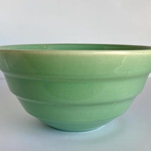 May include: A light green ceramic mixing bowl with a wide rim and a gently sloped, ribbed design. The bowl has a glossy finish and a smooth interior. The bowl is a kitchenware item.