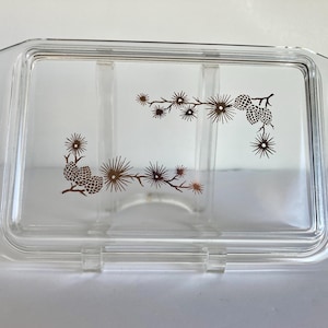 May include: Clear rectangular glass baking dish lid with a brown pinecone and branch design. The lid has a raised edge and is designed to fit a rectangular baking dish. The design is symmetrical.