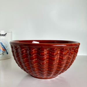 May include: A large, brown ceramic bowl with a wavy, textured design. The bowl is empty and appears to be made of a thick, durable material.