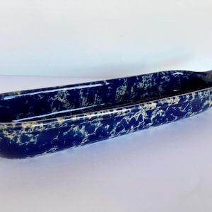 May include: A long, oval ceramic serving dish with a handle. The dish is a deep blue colour with a speckled, off-white pattern. The handle has a hole for hanging. Suitable for serving appetizers or snacks. Length approximately 30 cm.