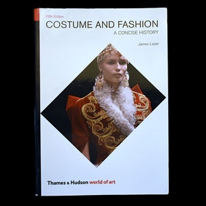 以下が含まれることがあります： ジェームズ・レイバー著「Costume and Fashion: A Concise History」というタイトルの本。表紙には、精巧な赤と金の衣装を着た女性が描かれています。「Thames & Hudson world of art」というテキストが下にあります。第5版です。