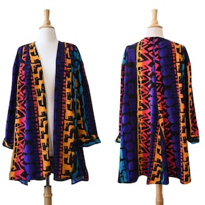 May include: An open-front jacket featuring a vibrant, multi-colored geometric and abstract pattern in shades of purple, orange, pink, teal, and black. The garment has long sleeves and a straight hem, displayed on a mannequin from front and back views.
