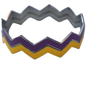 Op de afbeelding: Een zilverkleurige armband met een zigzagontwerp. De armband heeft een geel en paars emaillepatroon. De armband is een modeaccessoire.