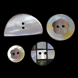 May include: Four iridescent mother-of-pearl buttons in various shapes. Includes a half-moon shape with two holes, a round button with a flower-shaped center, another small flower-shaped button, and a square-patterned button.