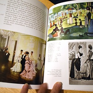 以下が含まれることがあります： 歴史的なファッションのイラストが掲載された開いた本。ある画像は、フォーマルな服装の人々がいる舞踏会のシーンを描いています。別の画像は、人物と犬がいる公園のシーンを示しています。3番目の画像は、ドレスを着た2人の女性を示しています。