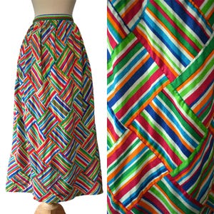 May include: A long, colourful skirt with a vibrant striped pattern in red, green, blue, orange, and white. The skirt's design features a woven or basket-weave effect, creating a unique visual texture. The waistband is a solid green with a thin stripe.