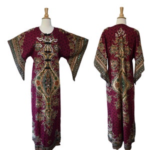 May include: A long, burgundy caftan dress with an ornate, colorful floral pattern. The dress features wide sleeves, a round neckline, and embellishments down the front. The sleeves and neckline are trimmed with black and gold detailing.