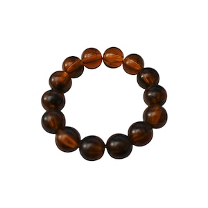 Può includere: Un braccialetto rotondo composto da grandi perline marrone scuro con venature ambra e nere. Le perline sono di dimensioni uniformi e infilate insieme, formando una forma circolare. Il braccialetto è su sfondo bianco.