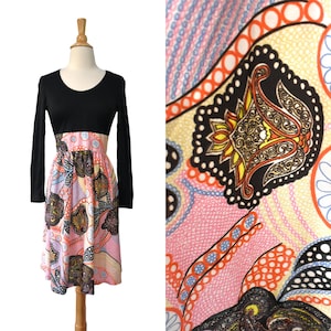 May include: A vintage dress with a black long-sleeved bodice and a patterned skirt. The skirt has a pink base with paisley and floral designs in orange, yellow, and blue. The dress is displayed on a mannequin.