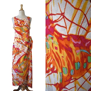 May include: Sleeveless, floor-length dress with a vibrant abstract pattern in orange, yellow, red, and white. The dress features a side tie detail and is displayed on a mannequin. The fabric's design is visible in a close-up shot.