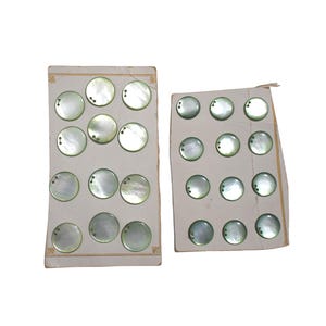 May include: Two vintage cards of iridescent, round mother-of-pearl buttons. Each button has two holes. The buttons are arranged in rows on aged, off-white cardboard. The cards have decorative gold trim.