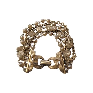 May include: Vintage gold-tone bracelet featuring multiple strands of faux pearls and clear, faceted beads. The bracelet has an ornate clasp with a decorative design. A classic piece of jewelry.