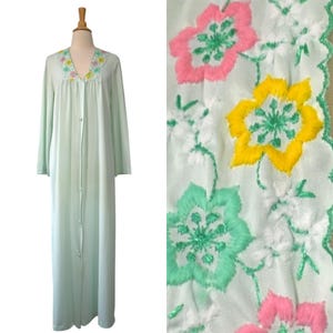 May include: A light green, long-sleeved robe with a button-up front and a floral embroidered neckline. The robe features a V-neck and a floor-length design. A close-up shows a white fabric with embroidered pink, yellow, and green flowers.