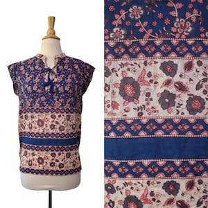 Könnte beinhalten: Ein ärmelloses blaues Oberteil mit einem Blumenmuster in Rosa und Weiß. Das Oberteil hat einen Schlüsselloch-Ausschnitt mit einem Quastenband. Der untere Teil des Oberteils hat ein breites blaues Band. Der Stoff auf der rechten Seite des Bildes zeigt das Muster.