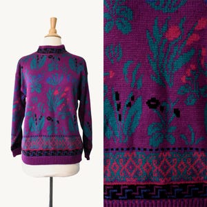 May include: A white ceramic mug with a black handle and the text "But First, Coffee" in a bold, black font. The mug is set against a blurred background, suggesting a cozy setting.