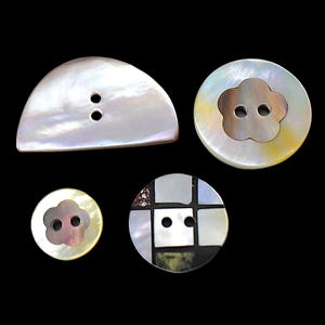 May include: Four mother-of-pearl buttons with iridescent surfaces. One is a semi-circle with two holes, two are circular with flower-shaped centers featuring two holes, and one is a circular button with a grid pattern of square inlays and two holes.