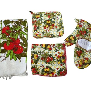 May include: A kitchen set featuring a white towel with red tomatoes and green leaves, a square pot holder, a square dishcloth, and an oven mitt. All items have a fruit and vegetable pattern on a light green grid background.