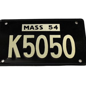 May include: Black metal license plate with white lettering. The plate reads "MASS 54 K5050".