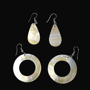 May include: A set of three earrings made of white mother of pearl. Two earrings are teardrop shaped and one is a circle with a hole in the center.
