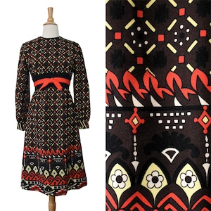 May include: A long-sleeved dress featuring a dark brown base with a geometric pattern in red, yellow, and white. The dress includes a solid black waistband with a bright red tie-front sash and a hemline decorated with stylized floral motifs.