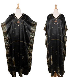 May include: Two black caftans on mannequins. The caftans have a V-neck and are decorated with gold and brown patterns. The fabric appears to be silky and flowing. The caftans are displayed on wooden mannequins against a white background.