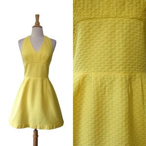 May include: A bright yellow sleeveless dress featuring a V-neckline and a fitted bodice that transitions into a flared skirt. The fabric has a distinct raised, repeating semi-circular scale pattern throughout the entire garment.