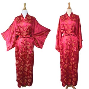 May include: A red satin robe with a gold floral pattern and a matching belt. The robe is displayed on a mannequin, showcasing its long sleeves and flowing design. The robe is a vibrant shade of red.