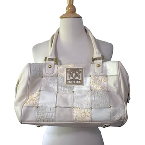 Puede incluir: Bolso de mano color crema con diseño patchwork. El bolso tiene forma rectangular, asas dobles y herrajes dorados. El patchwork incluye varias texturas y patrones, con un logotipo metálico en la parte delantera.