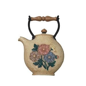 Pode incluir: Bule de cerâmica creme com um design floral em tons de rosa, azul e amarelo. O bule tem uma alça e um bico pretos e uma alça de madeira. O bule é um item decorativo.