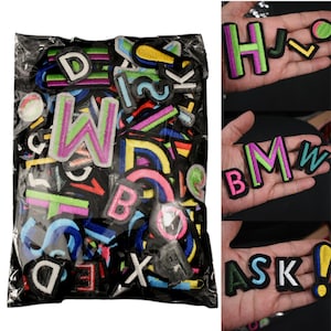 May include: A clear plastic bag filled with colorful embroidered letter patches. Individual patches are shown spelling out "H", "BMW", and "ASK". The patches feature various colors including green, pink, blue, and yellow, with black borders.