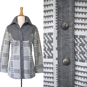 May include: A grey and white patterned jacket with a large collar and silver buttons. The jacket has a mix of geometric and textured designs. The close-up shows the intricate button details and the fabric's weave.