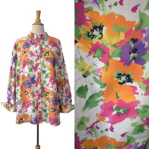 May include: A long-sleeved button-down shirt featuring a white base with a vibrant watercolor-style floral print in shades of orange, hot pink, purple, and green. The shirt has a standard collar, a front button placket, and cuffed sleeves.