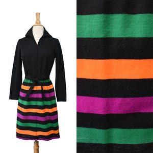 May include: A vintage black dress with long sleeves and a collared neckline. The dress features a striped skirt in green, orange, and purple. A black belt cinches the waist. The dress is displayed on a mannequin.