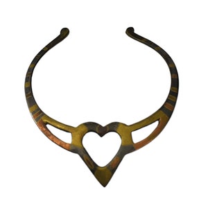May include: A rigid open-ended collar necklace featuring a central heart-shaped cutout. The metal band displays alternating segments of brass, copper, and dark oxidized silver tones, creating a multi-colored metallic finish throughout the piece.