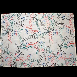May include: A rectangular, off-white scarf with a repeating pattern of cursive script in red, black, and green. Small blue and red heart-shaped clusters are scattered across the fabric. The word "amour" is visible.